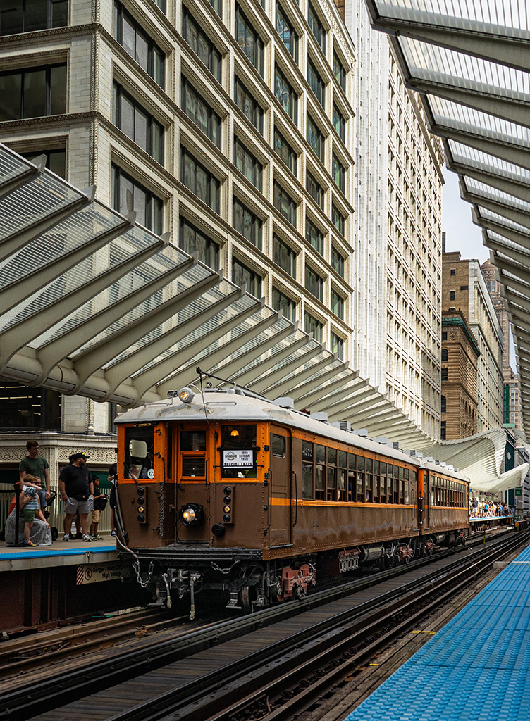 Train number 4272 of the 4000-Series is in the Washington and Wabash train station in downtown Chicago. There are skyscrapers behind the building.